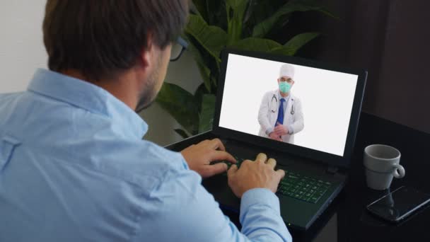 シニア男性医師は白い医療コート、聴診器、ヘッドセットを身に着けている遠くのビデオ通話を行います。古い大人の医師は、 Webチャットで患者をオンラインでカメラコンサルティングに話します。テレメディシンの概念. — ストック動画