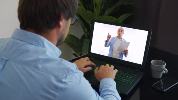 Estudiante joven viendo lecciones en línea y estudiando desde casa. Hombre tomando notas mientras mira la pantalla de la computadora después de profesor haciendo matemáticas en la videollamada. Hombre estudiante estudiando desde casa . — Vídeos de Stock