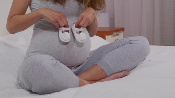 아기의 신발을 손에 쥐고 있는 행복 한 여인 . 엄마가 아기를 기다리고 있어. 임신 한 여자 아이를 낳는다. 임신. — 비디오