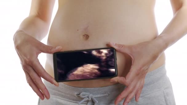 Une femme enceinte regarde une échographie sur un téléphone intelligent se frottant près de l'estomac. — Video