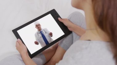 Kanepede uzanan ve Doktoruyla Tablet Bilgisayarda Video Sohbeti yapan Kadın.