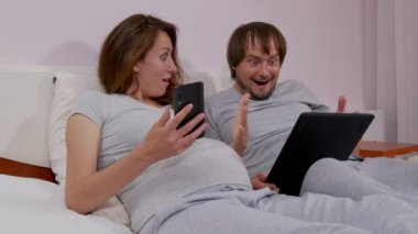 Mutlu çift ellerinde akıllı telefonla cep telefonu ekranlarına bakıyor, koltukta şaşırıyor, evde akıllı telefondan internet haberleri okumaktan zevk alıyor..