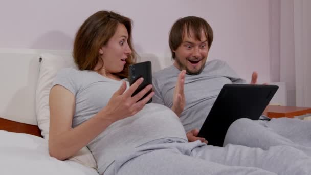 Glada par som håller smartphone tittar på mobiltelefon skärm titta på, bli förvånad på soffan, ha kul njuta läsa online nyheter i smartphone hemma. — Stockvideo