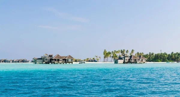 eautiful wooden villas, standing on stilts on little island in the middle of turquoise waters of the Indian Ocean, against the blue sky and green palm trees, Maldives. Travel and tourism concept