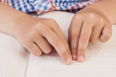 Kör çocuk Braille üzerinde yazılı bir kitap okuyor. 