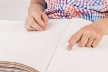 Kör çocuk Braille üzerinde yazılı bir kitap okuyor. 
