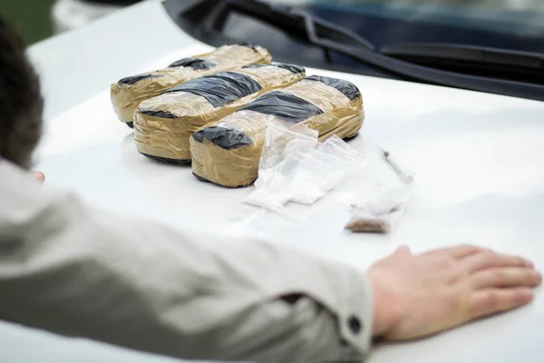 Vastzittende crimineel op de motorkap van een auto met pakketten van drugs. — Stockfoto