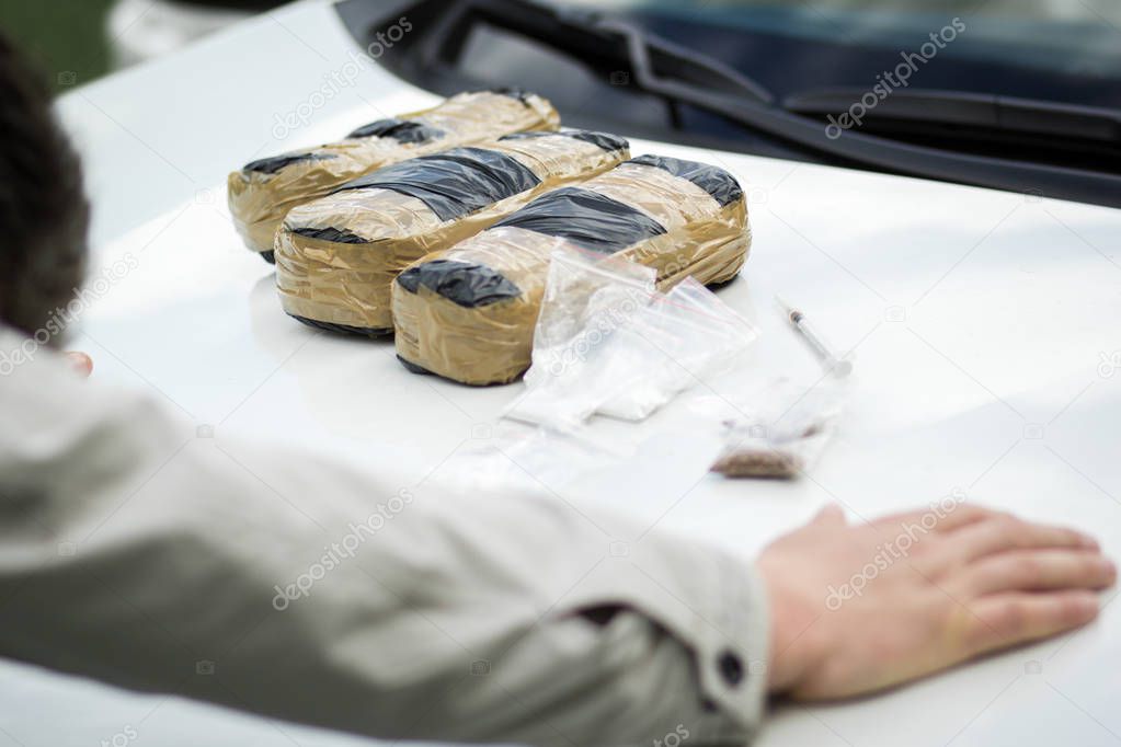 Detained criminal on the hood of a car with packets of drugs.