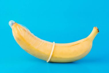 Mavi arka planda kondom ve muz yakın planda.