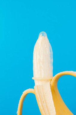 Mavi arka planda kondom ve muz yakın planda.