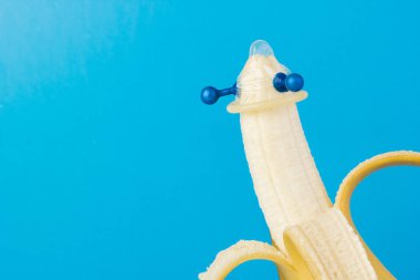 Mavi arka planda kondom ve muz yakın planda.