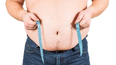 Adam göbeğini mezurayla ölçüyor.