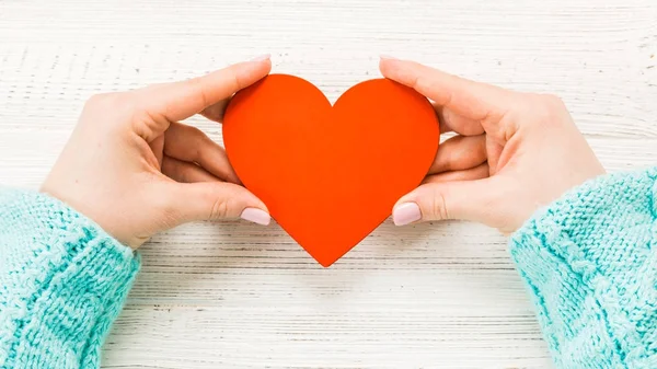 red heart in hands closeup on wooden background.