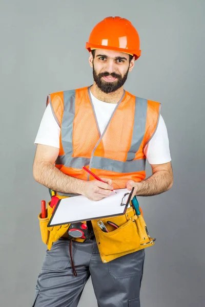 Um construtor em um capacete laranja em um fundo cinza sinais somethi — Fotografia de Stock