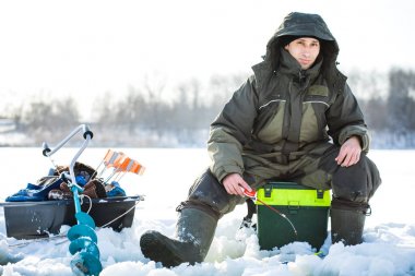 Genç bir adam bir delikten buzda balık tutuyor. Balık tutma kış