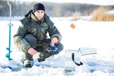 Genç bir adam bir delikten buzda balık tutuyor. Balık tutma kış