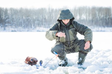 Genç bir adam bir delikten buzda balık tutuyor. Balık tutma kış