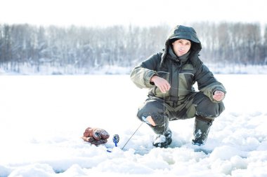 Genç bir adam bir delikten buzda balık tutuyor. Balık tutma kış