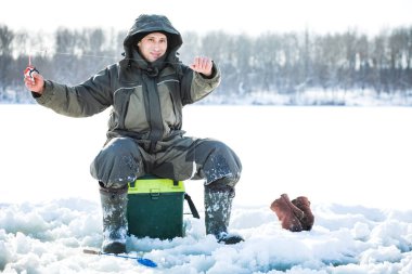 Genç bir adam bir delikten buzda balık tutuyor. Balık tutma kış