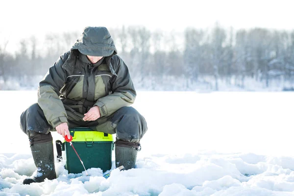 Ein junger Mann fischt aus einem Loch auf Eis. Winterfischen — Stockfoto