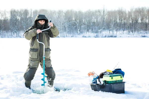 Рибалка свердлить дірку в льоду. зимова риболовля на задньому плані — стокове фото