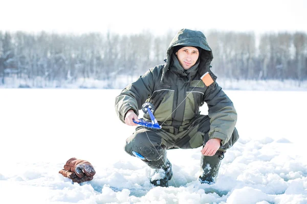 Genç bir adam bir delikten buzda balık tutuyor. Balık tutma kış