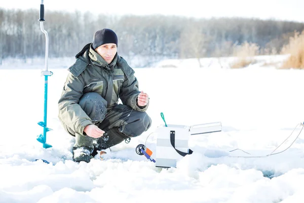 Ein junger Mann fischt aus einem Loch auf Eis. Winterfischen — Stockfoto