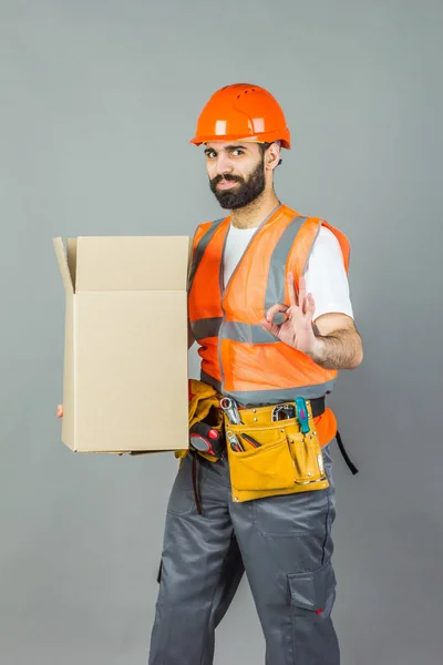 A man-builder in an orange helmet with a cardboard box in his ha — Stock Photo, Image