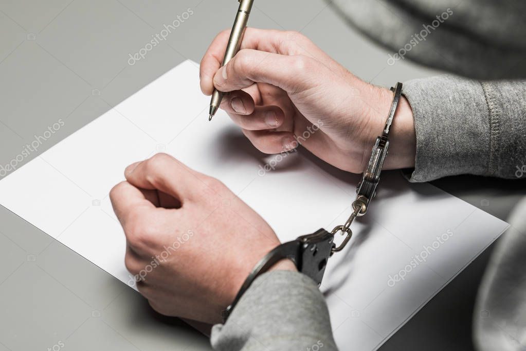 Hands of the criminal in handcuffs write a handle on paper. Sincere confession, request, statement. Justice.