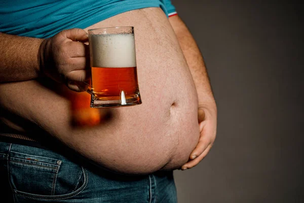 A man with a fat belly holding a glass of beer. On dark backgrou