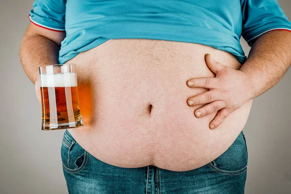 Un hombre con el vientre gordo sosteniendo un vaso de cerveza. Sobre fondo gris —  Fotos de Stock