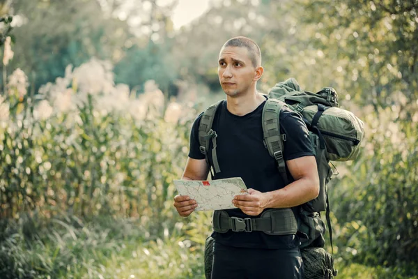 Man brunette tourist lost in the woods, holding a map, looking i