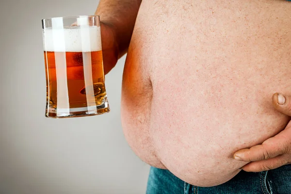 Un hombre con el vientre gordo sosteniendo un vaso de cerveza. Sobre fondo gris —  Fotos de Stock