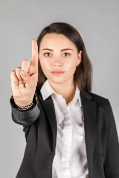 Mädchen in schwarzer Jacke auf grauem Hintergrund zeigt Finger — Stockfoto