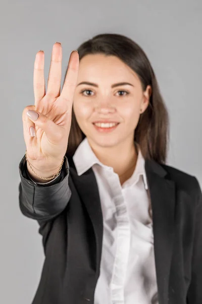 Mädchen in schwarzer Jacke auf grauem Hintergrund zeigt 3 Finger — Stockfoto