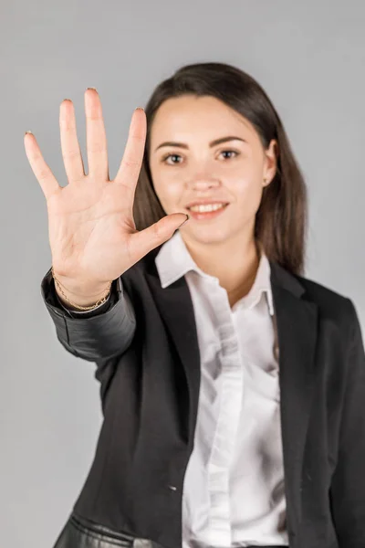 Mädchen in schwarzer Jacke auf grauem Hintergrund zeigt 5 Finger — Stockfoto