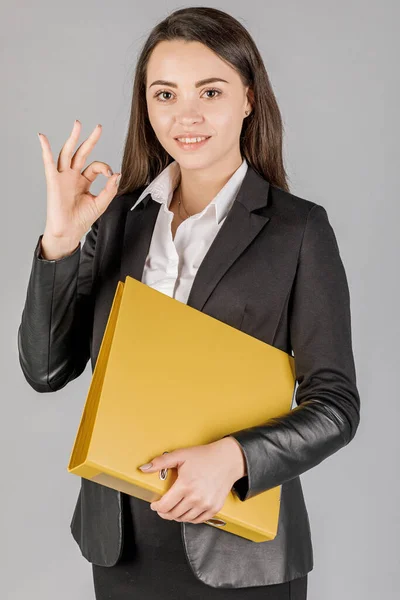 Young business woman in dark suite with file on grey background.