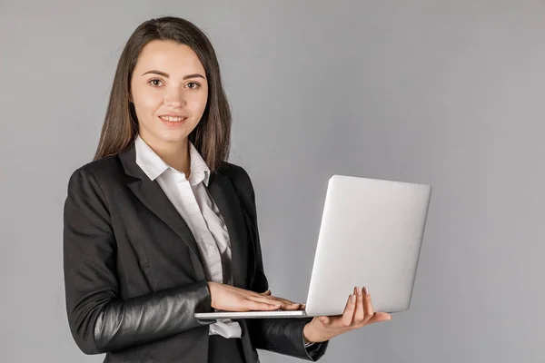 Young business woman in dark suite with laptop on grey backgroun