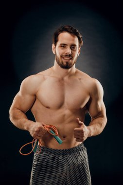 Yakışıklı bir erkek vücut geliştirici. Elinde iple karanlık bir arka planda.