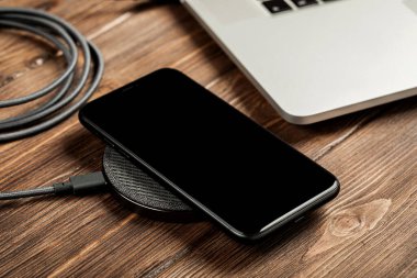 Kablosuz şarj şık bir ahşap masa üzerinde bilgisayarın yanında yatıyor.