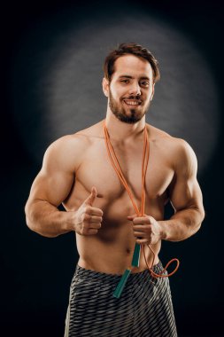 Yakışıklı bir erkek vücut geliştirici. Elinde iple karanlık bir arka planda.