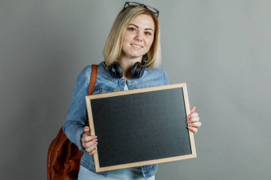 Güzel sarışın, gözlüklü, gri bir arkaplanda tek başına bir tahtası var.