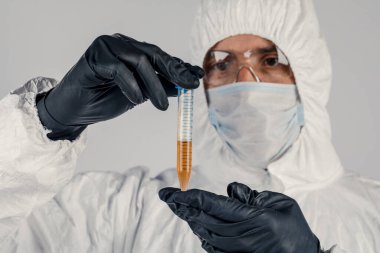 Bir adamın elinde test tüpü yakın plan, elinde kırmızı sıvı tutan tıbbi maskeli bir adam. Kan örnekleri, tıbbi ve kimyasal araştırmalar.