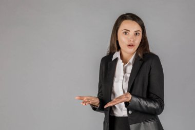 Gri arka planda, koyu renk süitte genç bir iş kadını. Ofis kavramı