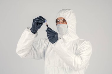 Bir adamın elinde test tüpü yakın plan, elinde kırmızı sıvı tutan tıbbi maskeli bir adam. Kan örnekleri, tıbbi ve kimyasal araştırmalar.