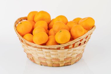 Beyaz arkaplanda biraz mandalina bulunan hasır sepet..