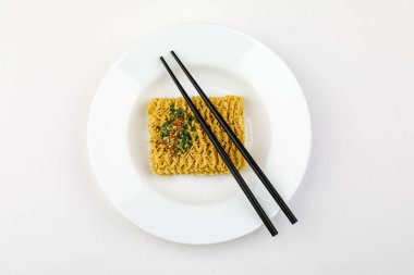 Beyaz arka planda yemek çubukları olan tabakta kuru erişte..