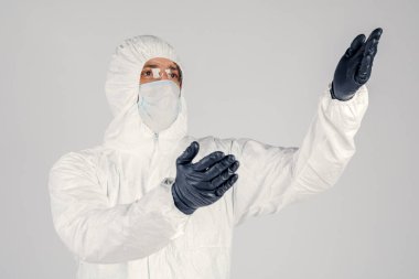 Tek kullanımlık anti-bakteriyel izolasyon giysisi içindeki bir insan epidemiyoloğu beyaz arka planda el hareketlerini gösteriyor. Salgın ve tıbbi konsept.