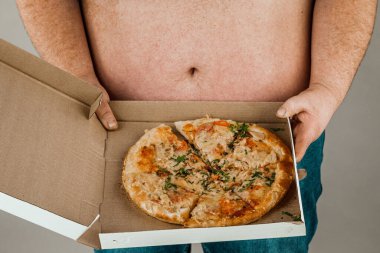 Gri arka planda pizza dilimi olan şişman adam, sağlıksız yemek kavramı..