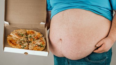 Gri arka planda pizza dilimi olan şişman adam, sağlıksız yemek kavramı..